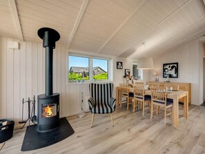 A cozy room with a wood-burning stove, a dining area with wooden furniture, and large windows offering a view of the outside.