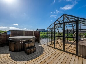 En træterrasse med jacuzzi, et glashus og udsigt over landskabet.