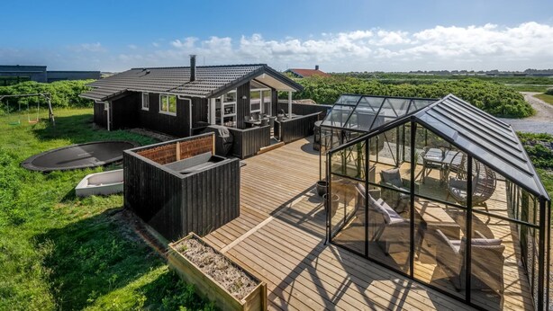 A wooden deck with a glass-enclosed area, a small house with a sloped roof, and a swing set.