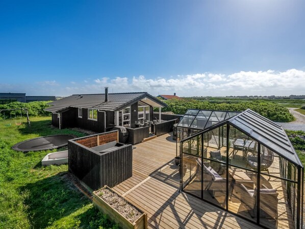A modern house with a deck, a glass greenhouse, and a view of the countryside.