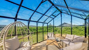 A glass-enclosed outdoor space with wicker furniture and a view of greenery.
