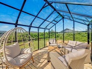 A glass-enclosed patio with wicker furniture and a hanging chair.