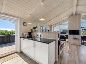 A modern kitchen with a large island, a dining area with a TV, and a view of the outdoors.