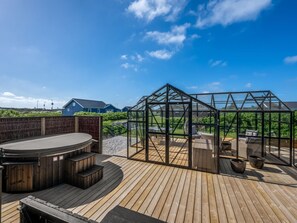 En træterrasse med et drivhus i glas, udendørs møbler og udsigt til huse i baggrunden.
