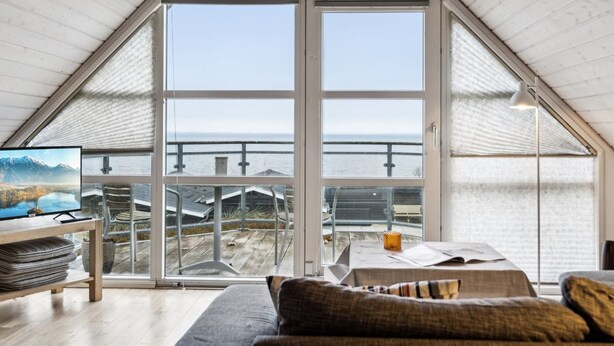 Un dormitorio estilo loft moderno con un tragaluz grande, vista al mar y un rincón de descanso acogedor.