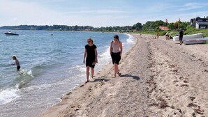 Una playa con gente caminando, un bote en el agua y casas al fondo.