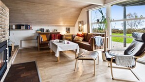 Un salón acogedor con chimenea, techo de madera y ventanas amplias que ofrecen vistas al exterior.
