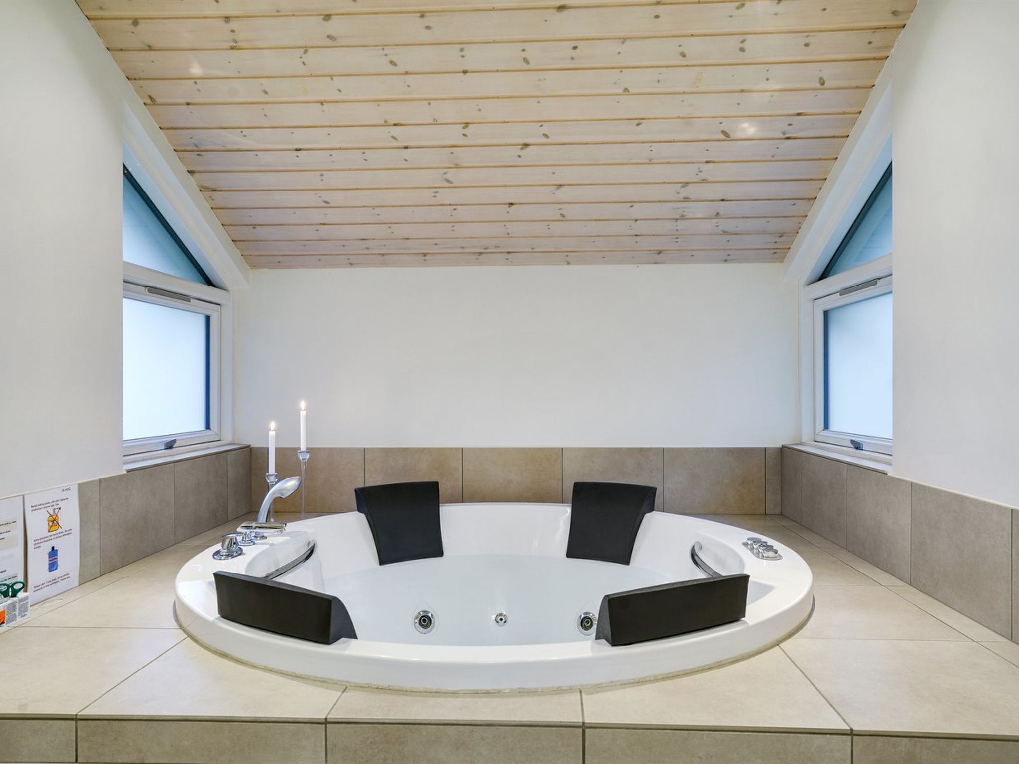 A modern spa room with a circular hot tub, two windows, and a wooden ceiling.