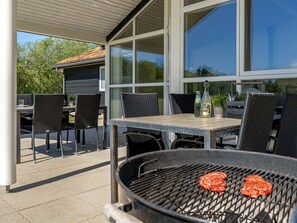 Eine Terrasse im Freien mit Grill, Esstisch und Stühlen.
