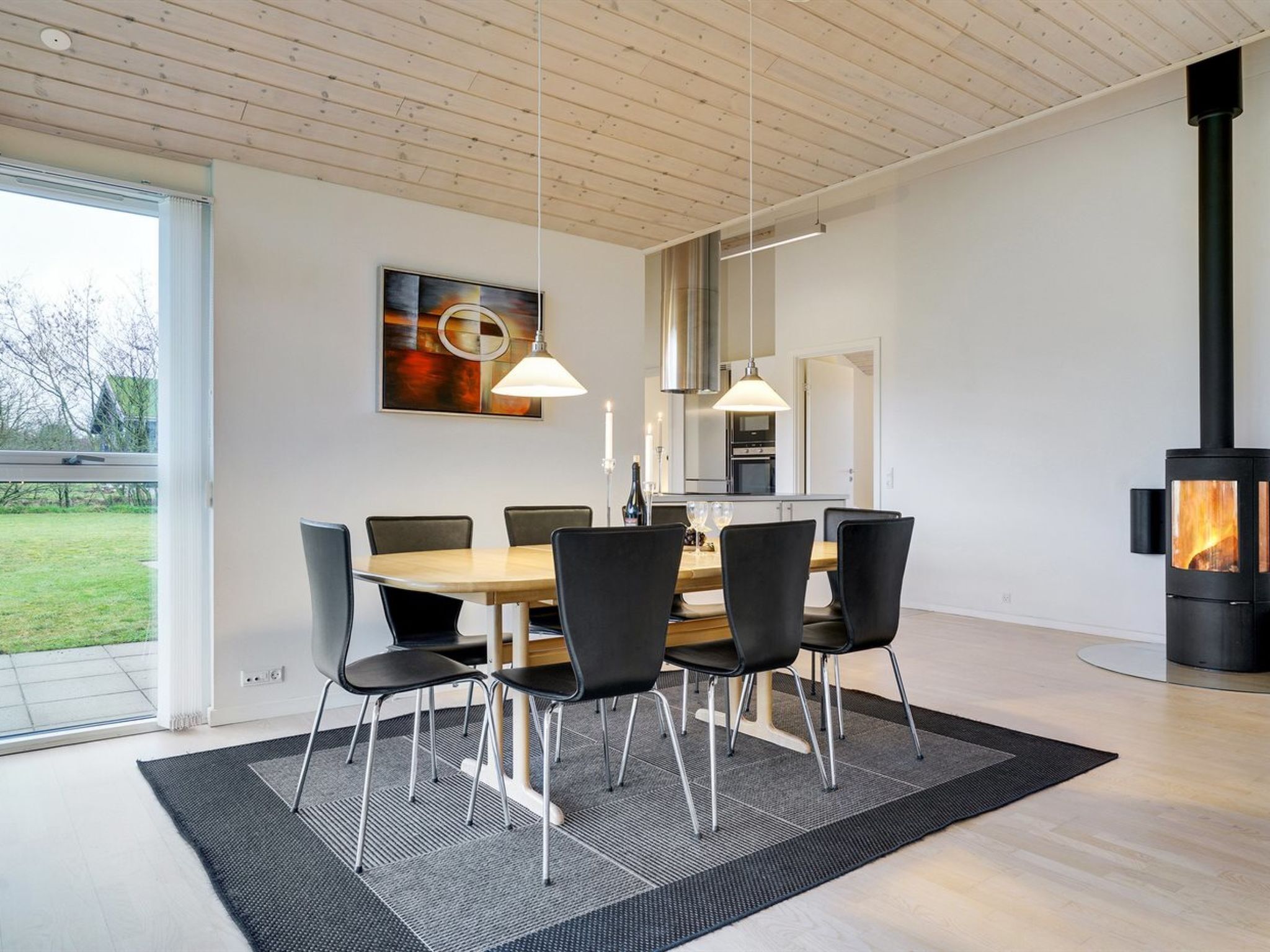 Ett modernt matområde med ett träbord och stolar, en hängande lampa och en svart spis.