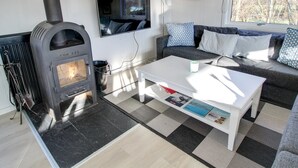 Ein modernes Wohnzimmer mit Kaminofen, einer Couch mit gemusterten Kissen, einem Flachbildfernseher und einem Fenster mit Blick auf Bäume.