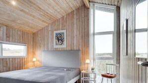 A bedroom with a bed, a bedside table, a chair, and a window with a view. - "Kalervo" - 100m from the sea by Interhome (Pandrup)