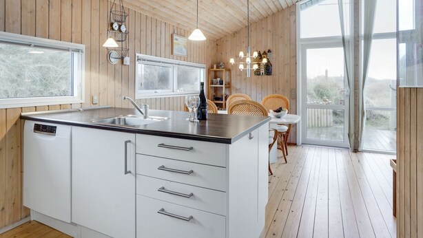 A modern kitchen with wooden walls, a large island with a sink, and a dining area with wicker chairs. - "Kalervo" - 100m from the sea by Interhome (Pandrup)