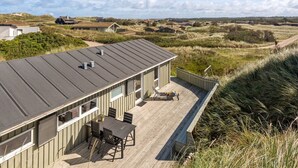 A modern house with a flat roof, a deck with a table and chairs, and a view of the surrounding landscape. - "Kalervo" - 100m from the sea by Interhome (Pandrup)