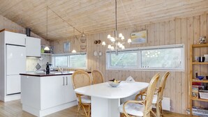 A modern kitchen with white cabinets, a central island, wicker chairs, and a dining table. - "Kalervo" - 100m from the sea by Interhome (Pandrup)