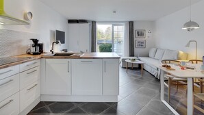 Cocina moderna con armarios blancos, una cafetera y un comedor con mesa y sillas.