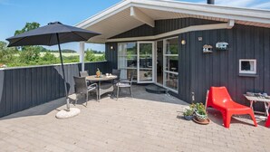 Een overdekt terras met een tafel, stoelen, een rode stoel en potplanten.