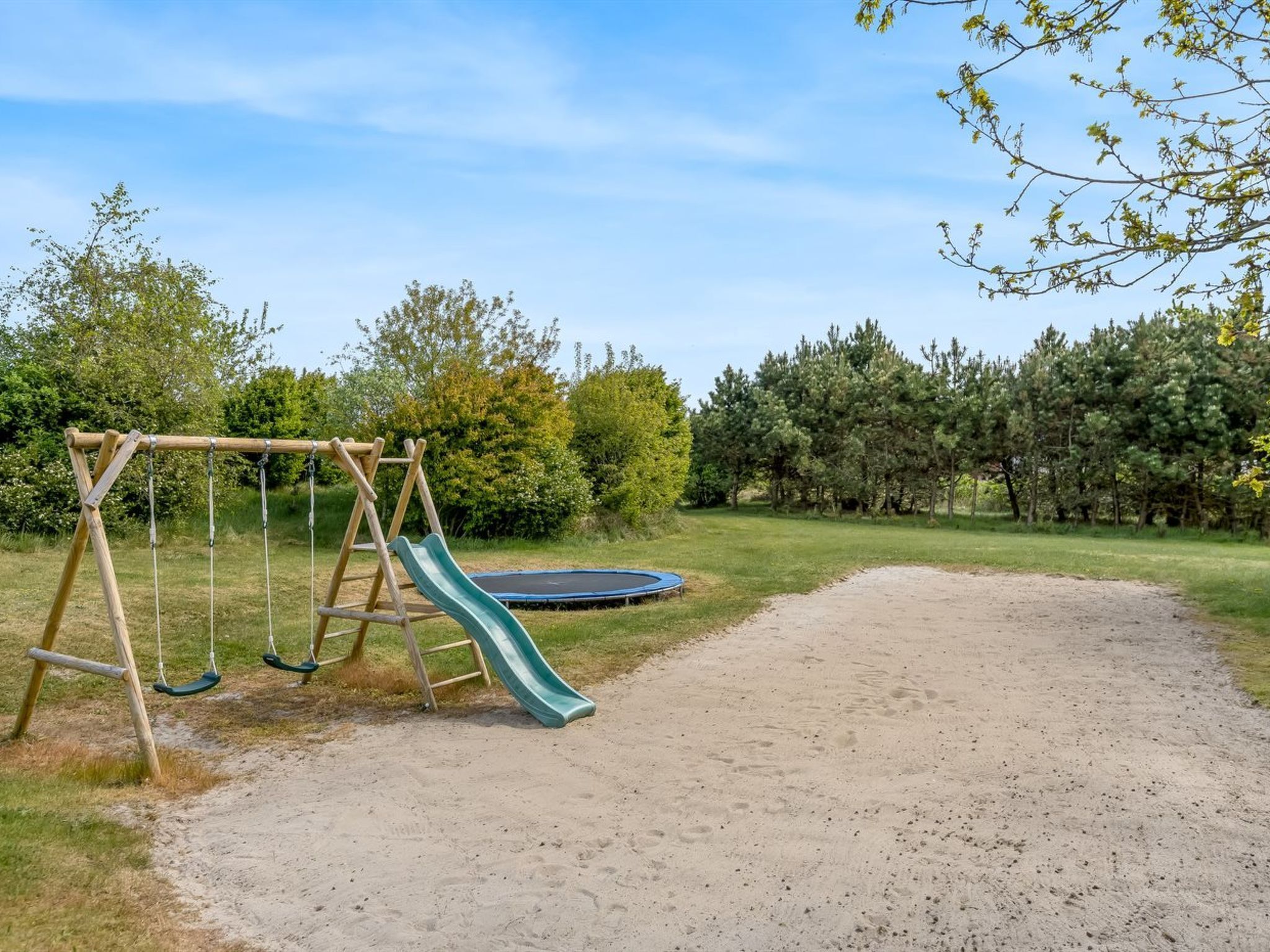 Un parque infantil con columpios y un tobogán, rodeado por un sendero de tierra y vegetación.