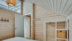 A bedroom with a bed, wooden walls, a white wardrobe, and a hanging light fixture.