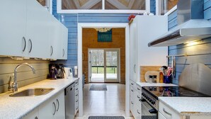 A modern kitchen with white cabinets, stainless steel appliances, and a large window overlooking a deck.