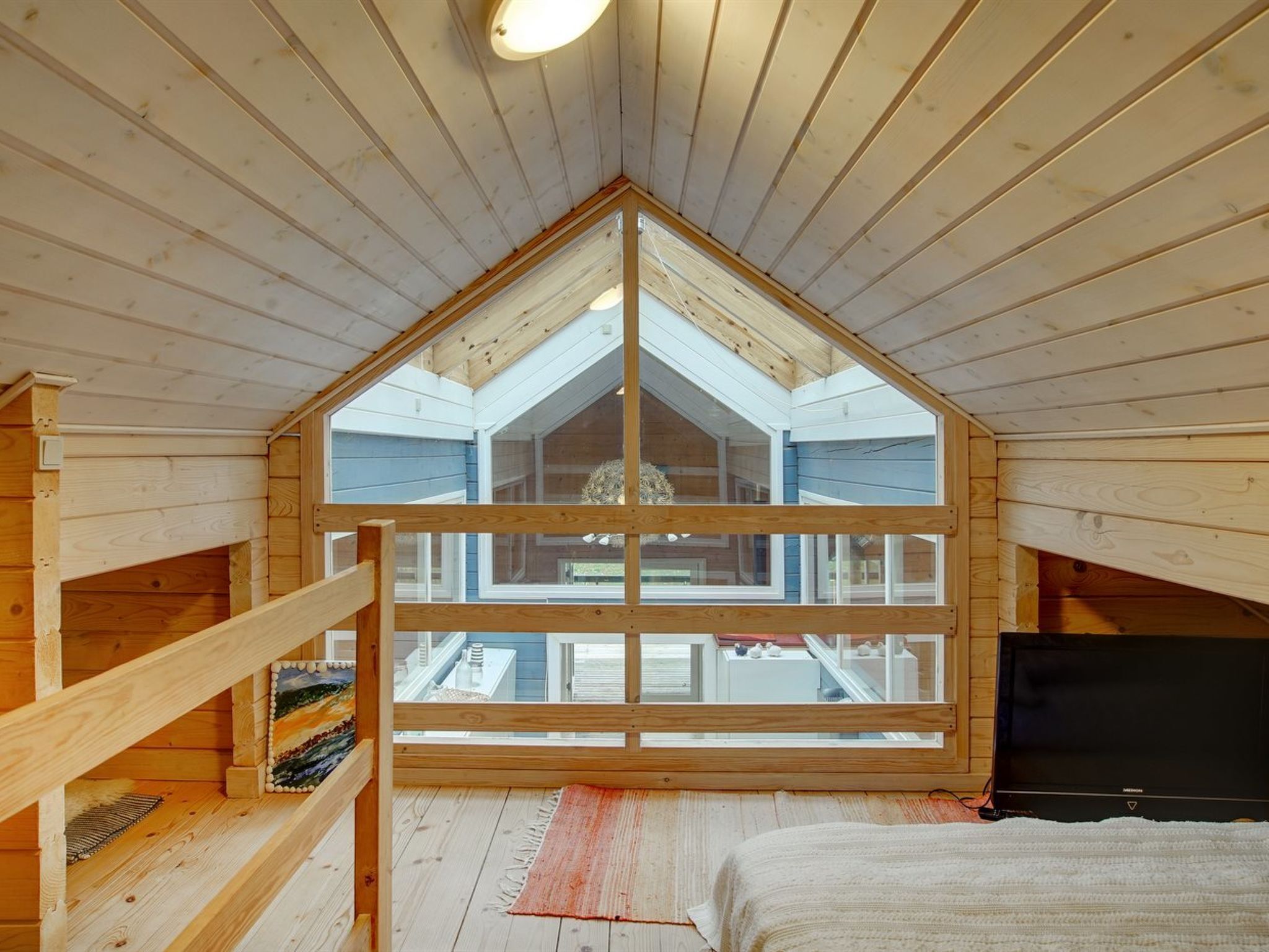 A cozy attic bedroom with a sloped ceiling, a large window, and a bed.