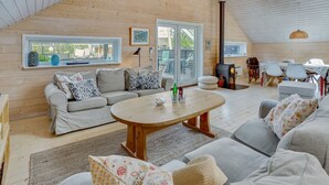 A cozy, well-lit room with a wooden ceiling, a sofa set, a round coffee table, and a dining area with chairs and a table.