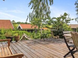A wooden deck with outdoor furniture, including a bench and chairs, surrounded by greenery and trees.