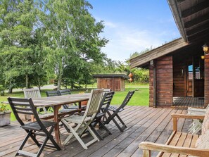 A wooden deck with a table and chairs, a small shed, and a building with a porch.