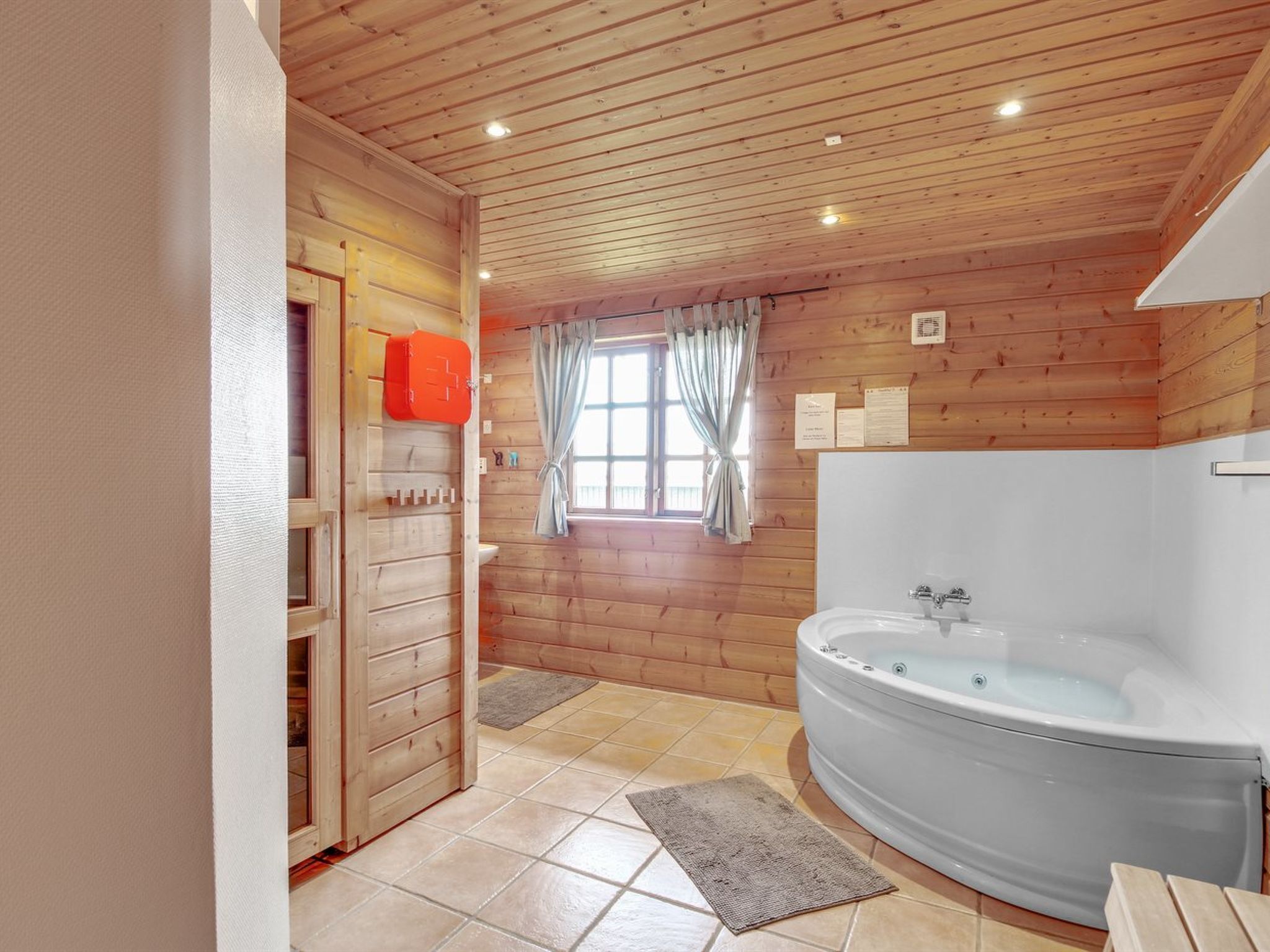 Une salle de bain rustique, avec une grande baignoire, des murs en bois et une fenêtre agrémentée de rideaux.