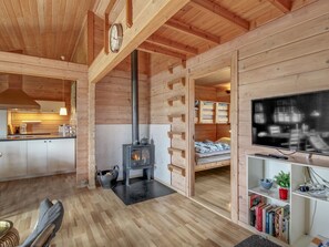 A cozy cabin interior with a wooden interior, a fireplace, a kitchen area, and a living room with a television and bookshelves.