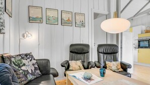Una sala moderna con un sofá, dos sillones de cuero negro, una mesa de centro y una pared con cuadros de un paisaje urbano.