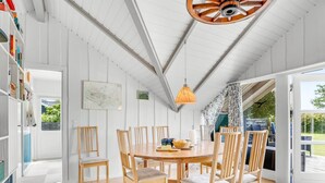 Comedor con mesa y sillas de madera, una lámpara colgante y vistas al exterior a través de un ventanal.