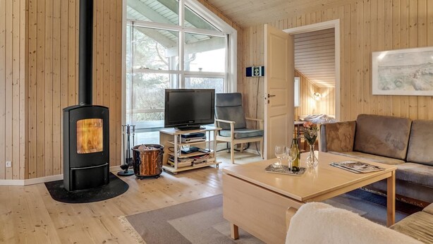 Ein gemütliches Wohnzimmer mit großem Fenster, Kamin, Fernseher und einer bequemen Sitzecke.