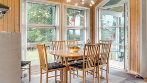 Ein Zimmer mit Holzwänden, einem runden Tisch und Stühlen, großen Fenstern und einer Deckenleuchte.