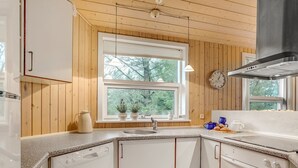 Eine kompakte Küche mit Holzvertäfelung, einem Fenster mit Pflanzen, einer Uhr und einem modernen Herd.