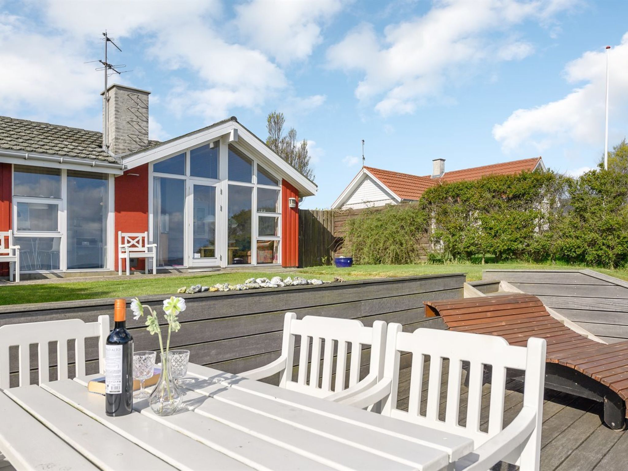 Eine Terrasse mit weißen Möbeln, einer Weinflasche und einem Glas.
