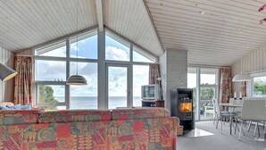 A spacious living area with a large sofa, a fireplace, a dining table with chairs, and large windows offering a view of the sea. - "Keti" - 5m from the sea by Interhome (Nyborg)