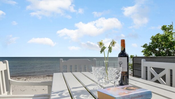 A white wooden table with a bottle of wine, two glasses, and a book on a beach with a view of the sea. - "Keti" - 5m from the sea by Interhome (Nyborg)