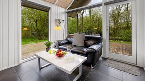 A modern living room with a black leather sofa, a white coffee table with fruit and glasses, and a view of a wooden deck and greenery outside. - "Ketilbiorn" - 1.2km to the fjord by Interhome (Hemmet)