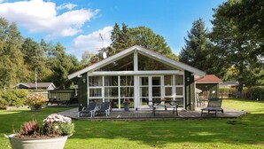 Een tweelaags huis met een overdekt terras, een groot raamfront en een klein terrasje met stoelen.