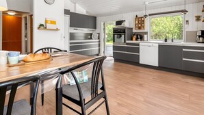 Een moderne keuken met grijze kastjes, een houten eettafel en een klok aan de muur.