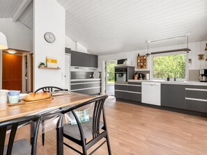 A modern kitchen with grey cabinets, a wooden dining table, and a clock on the wall. - "Hermand" - 700m from the sea by Interhome (Glesborg)