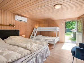 A room with wooden walls and ceiling, a bunk bed, a single bed, a desk, and a chair.