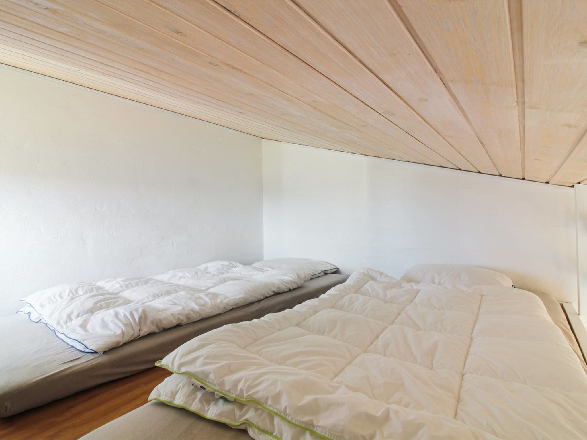 Een kleine eenpersoonskamer met een houten plafond en witte muren.