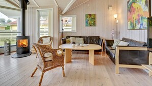Een gezellige woonkamer met een houtkachel, rieten stoelen, een bank en een schilderij aan de muur.