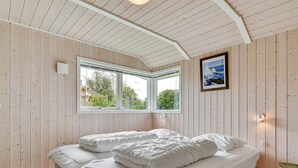 Een kamer met houten wanden en plafond, een bed met wit beddengoed, een raam met uitzicht op groen, en een ingelijste foto aan de muur.