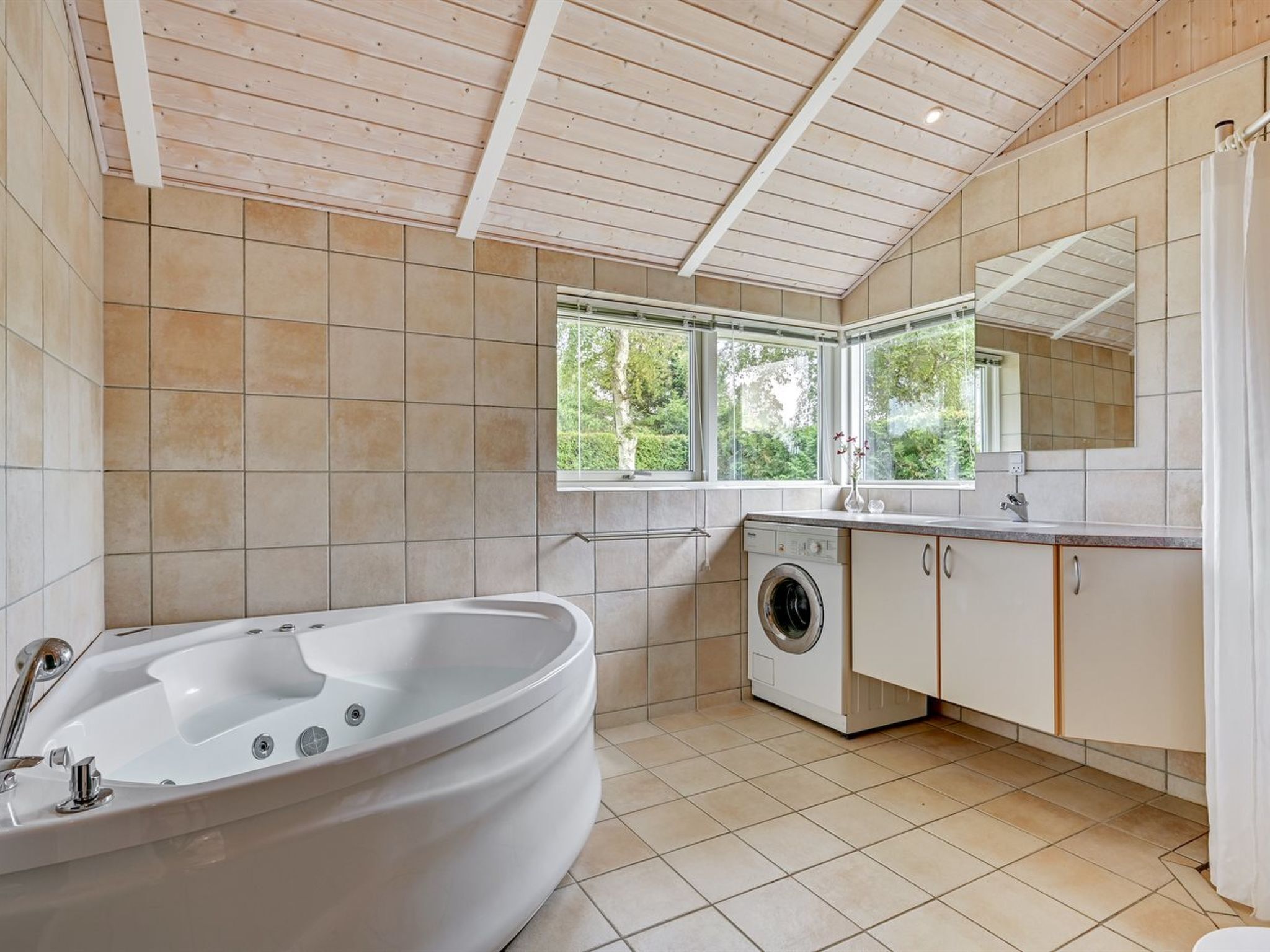 A modern bathroom with a freestanding bathtub, a washing machine, and a large mirror.