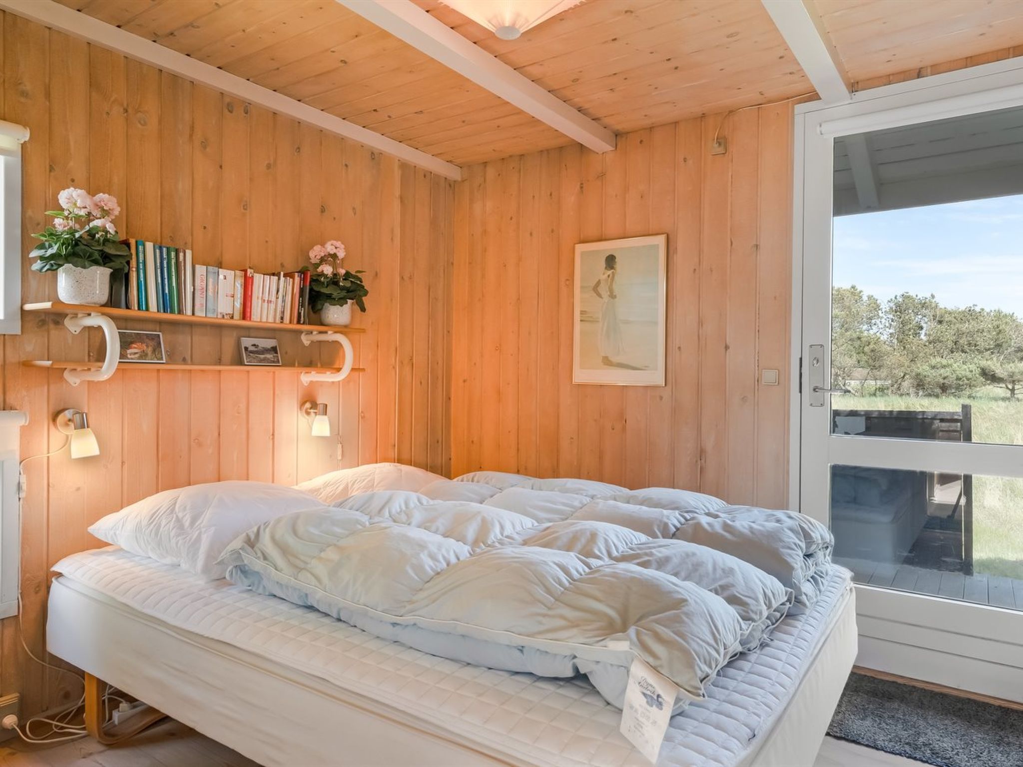 Ein Schlafzimmer mit Holzwänden, einem Bett, einem Bücherregal und einem Fenster mit Blick.