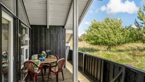 Een overdekt buitengebied met een tafel en stoelen, een raam met lamp, en uitzicht op een boom en gras.