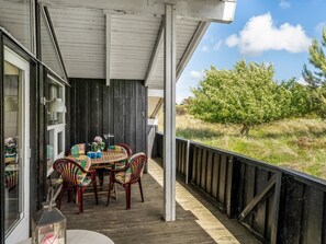 A covered outdoor area with a table and chairs, a window with a lamp, and a view of a tree and grass.